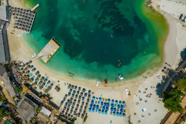 Rajskie **Albania wakacje**! Widok z lotu ptaka na turkusowe morze, piaszczystą plażę z leżakami i parasolami, drewniane molo i łodzie.