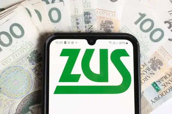 Telefon z logo ZUS na tle banknotów 100 zł. Czas na opłacenie składek ZUS.